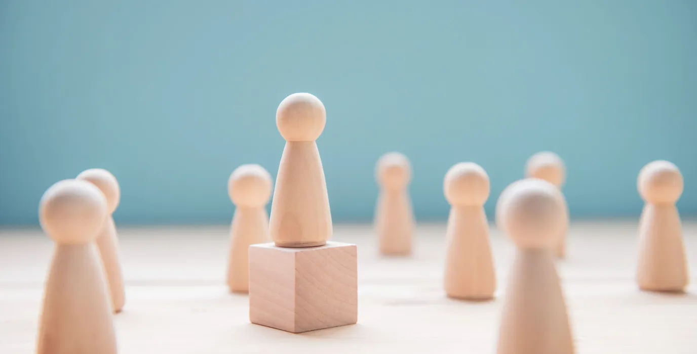Multiple wooden figures that are symbolic of people with one of the pieces elevated on a wooden block