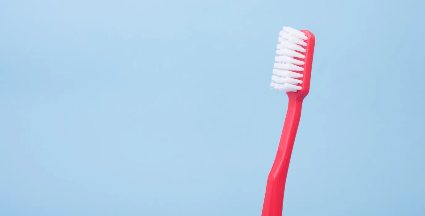 a pink toothbrush with white bristles in front of a blue background