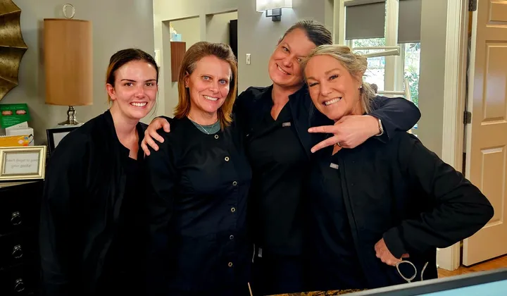 Four practice team members in dark scrubs posing together at a front desk