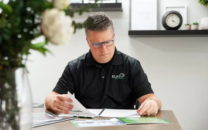 Phil Cole reading documents at a desk with a clock on the shelf behind him