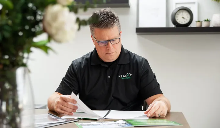 Phil Cole reading documents at a desk with a clock on the shelf behind him