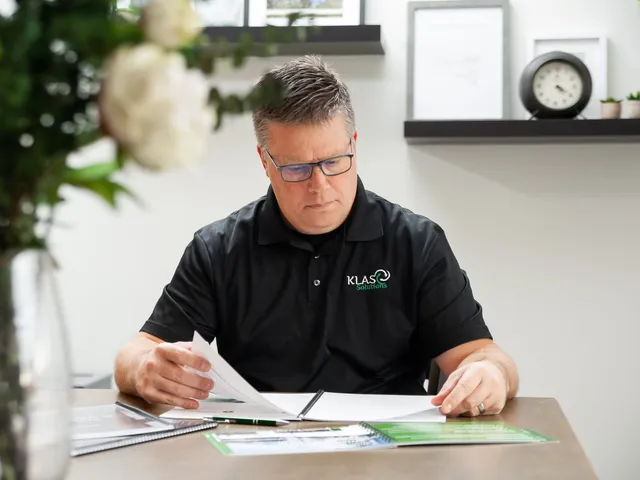 Phil Cole reading documents at a desk with a clock on the shelf behind him